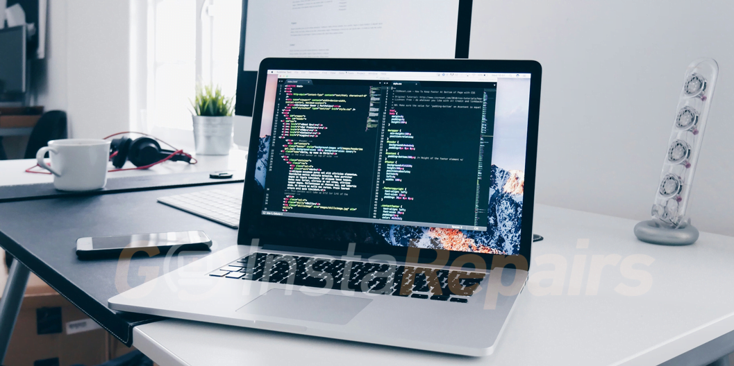 A MacBook with lines of code on its screen on a busy desk